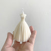 Ivory bridal wedding dress-shaped candle with fitted bodice and full pleated skirt held in hand.